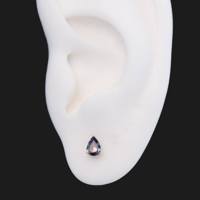 A Fiat Lux 3 Prong Pear Grande - Alexandrite earring in a three-prong flatback setting worn on an earlobe.