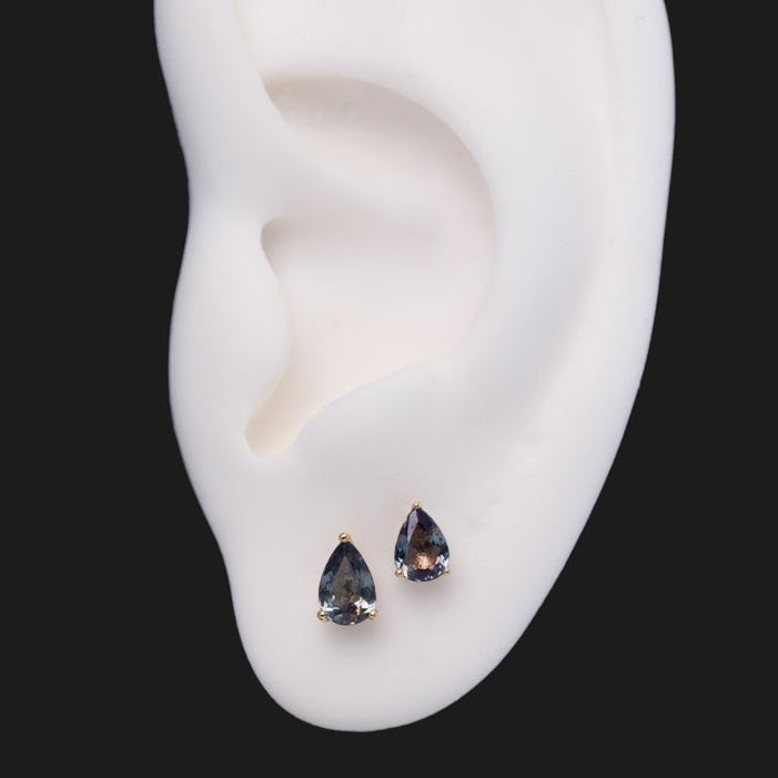 Fiat Lux 3 Prong Pear Grande - Alexandrite stud earrings, featuring two pear-cut, prong-set gems on a white ear model.