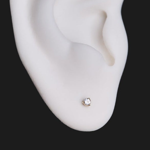 A white ear model wears Fiat Lux’s 3 Prong Round Colored Gem (2mm) stud, shown on a solid black background.