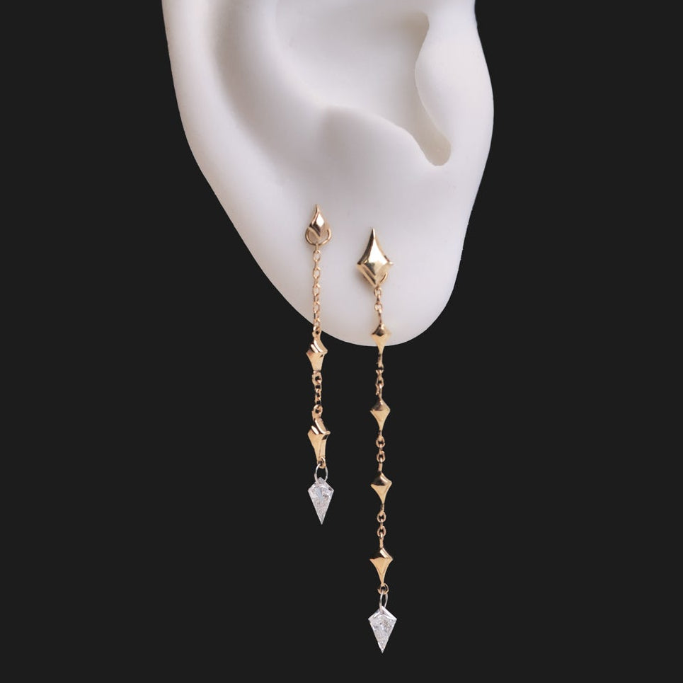 Fiat Lux Constellation Kite Dangle earrings: two 14K gold chains on a mannequin ear with north star charms and clear stones.