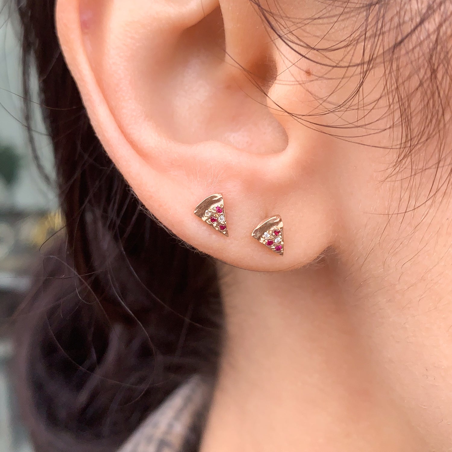 Close-up of ear with two Fiat Lux Pizza Studs, 14k gold earrings set with red stones and white diamond accents.
