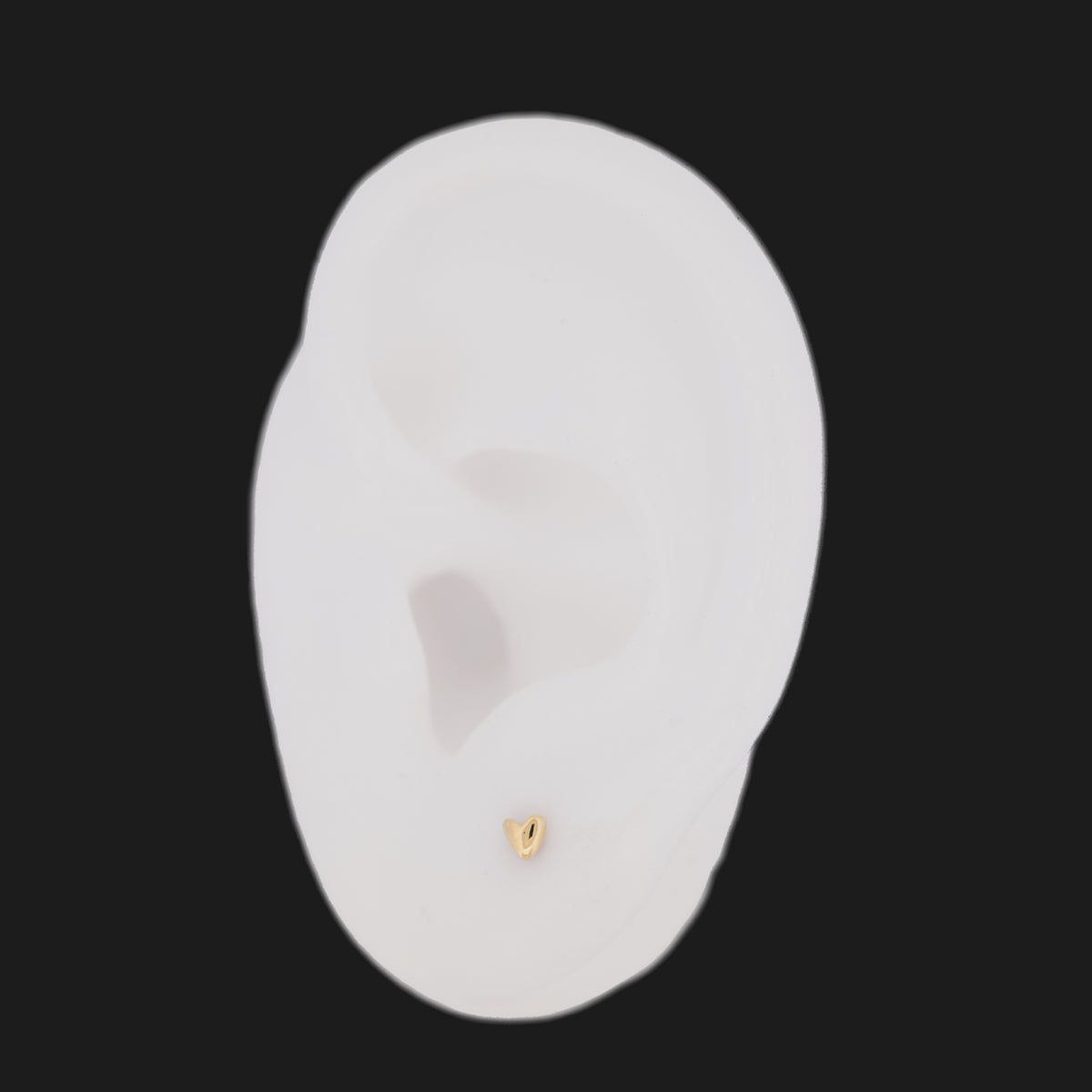 A Fiat Lux Petite Puffy Heart (3mm) 14K gold stud earring on a white ear model.