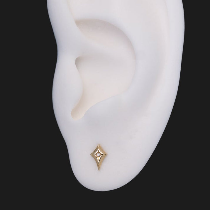 A Fiat Lux Classic Radiant North Star 14K gold diamond-shaped stud earring with a single central stone in an earlobe.