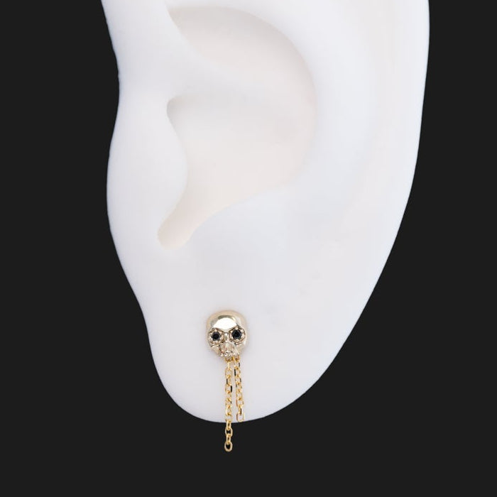 The Skull Stud - Petite by Fiat Lux on a white mannequin ear with chain, set against a solid black background.