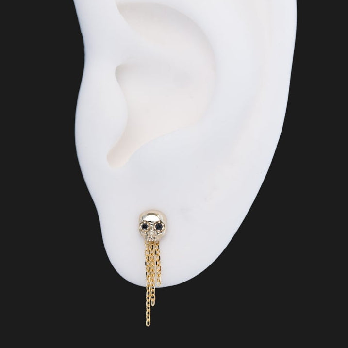 A Fiat Lux Three-Chain Dangle 14K gold skull stud earring with three delicate dangling chains, shown on a model ear.