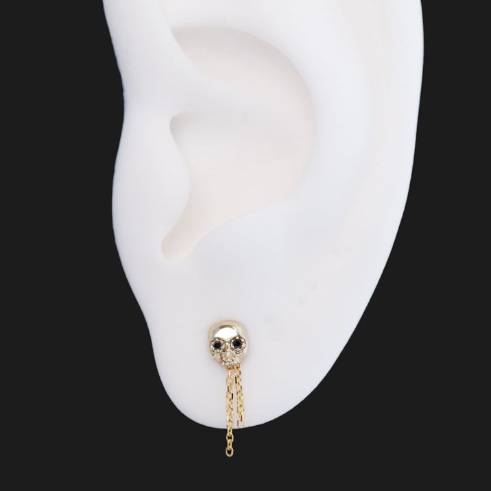 Fiat Lux Two-Chain Dangle gold skull earring with two short 12mm chains on a white ear model.