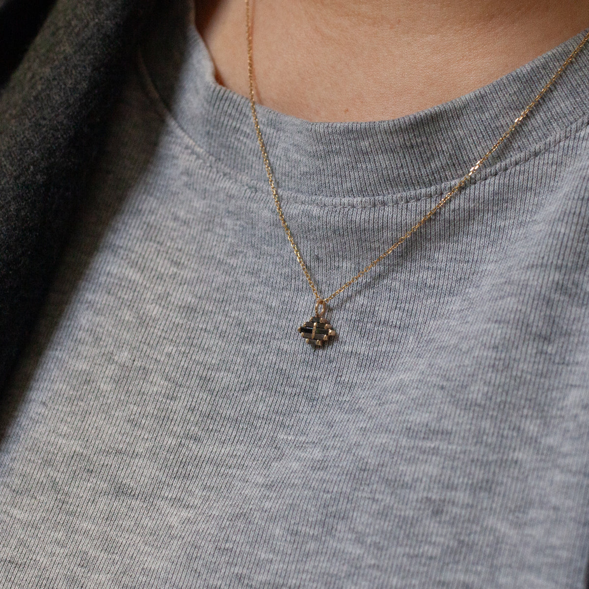 A small, geometric Arcadia Necklace with black diamonds hangs from a thin 14k gold chain around a person’s neck.