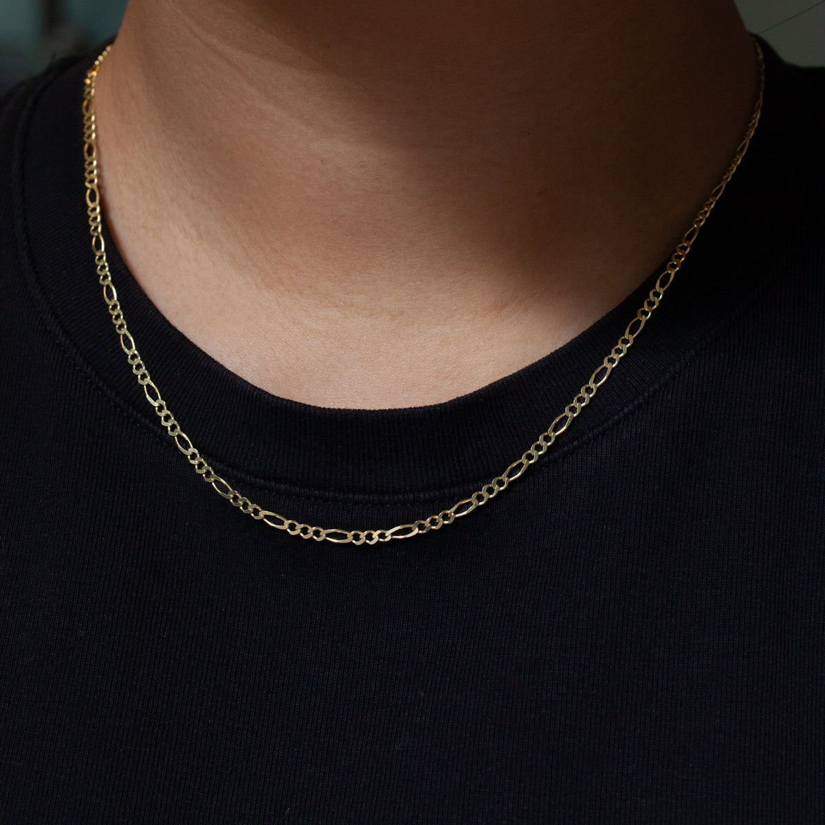 A Classic Figaro Chain by Fiat Lux rests on someone wearing a plain black shirt.