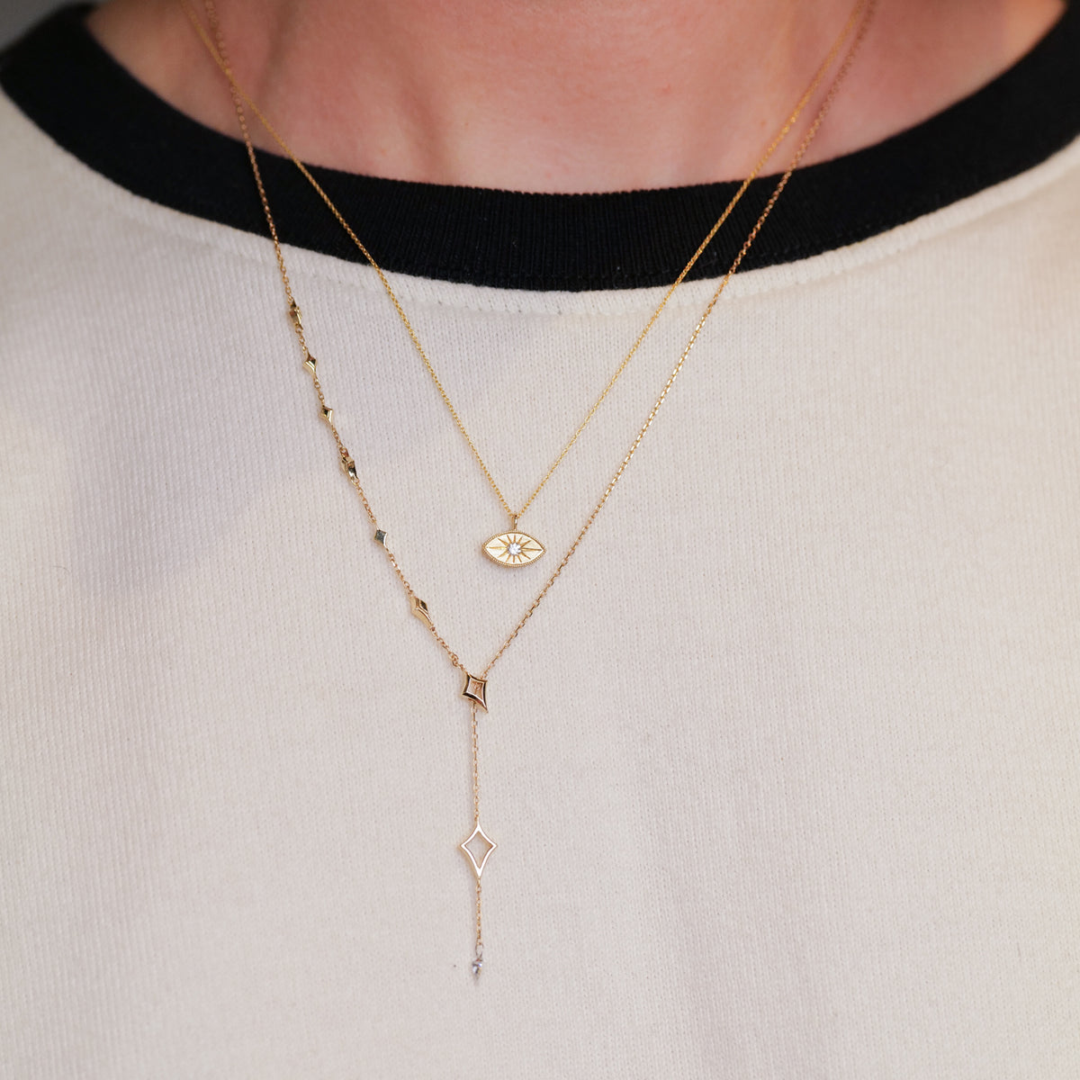 Fiat Lux’s North Star Lariat Necklace with white diamonds shines over a black-and-white crew neck shirt.