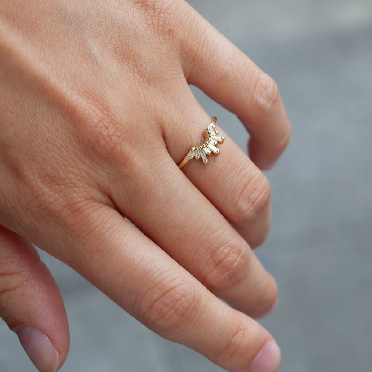 A hand wears the Fiat Lux Short Meridian Ring, 18k gold with small clear stones in a curved, clustered design.