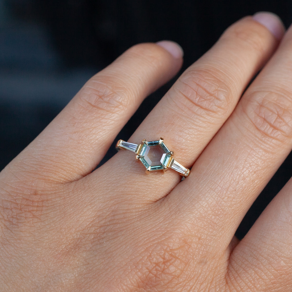 Fiat Lux Grande Calliope ring with a 1.50ct hexagonal seafoam green Montana sapphire and two baguette diamonds on a finger.