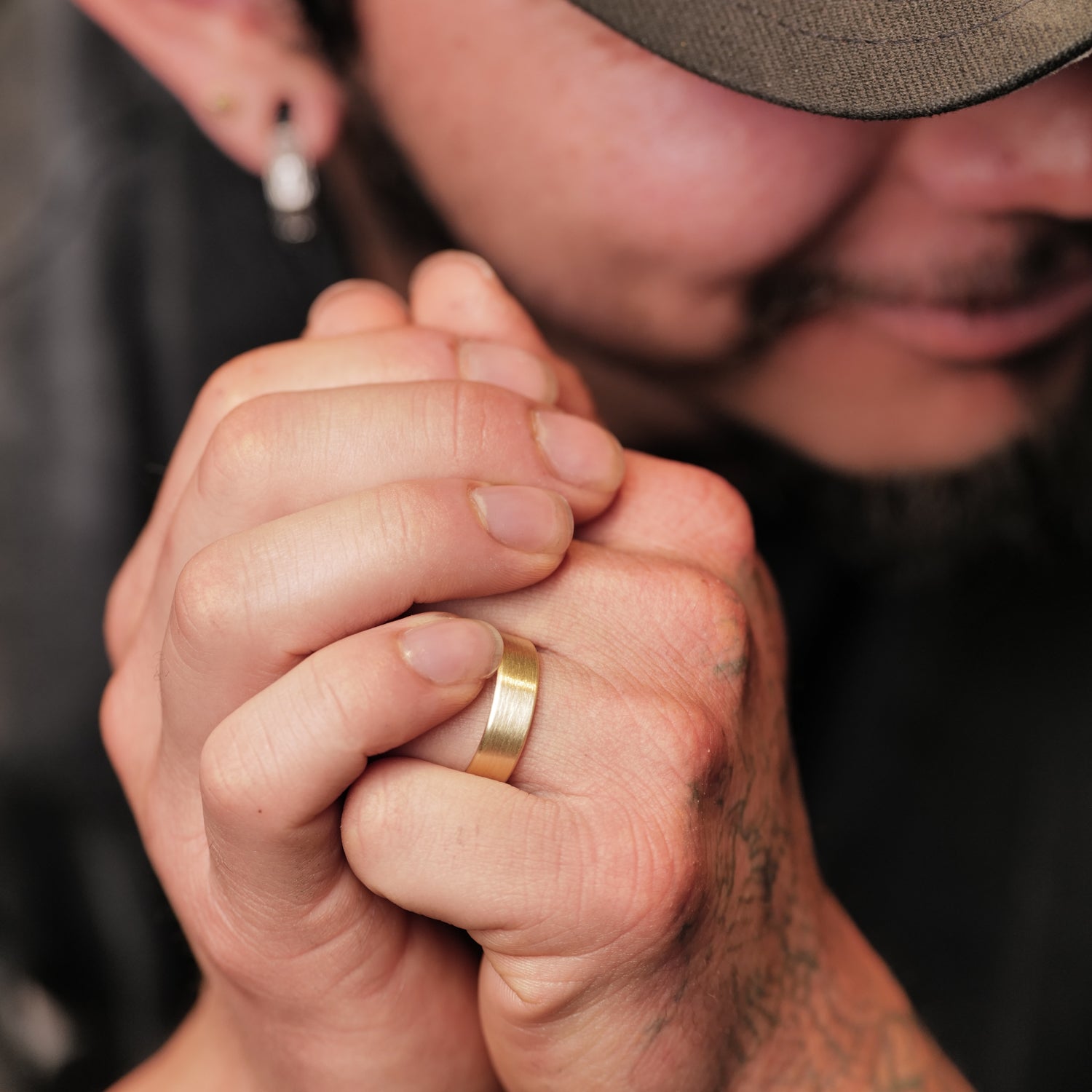 A close-up of hands wearing the Fiat Lux Classic Flat Band (6mm) in 18k gold, with a blurred face behind.