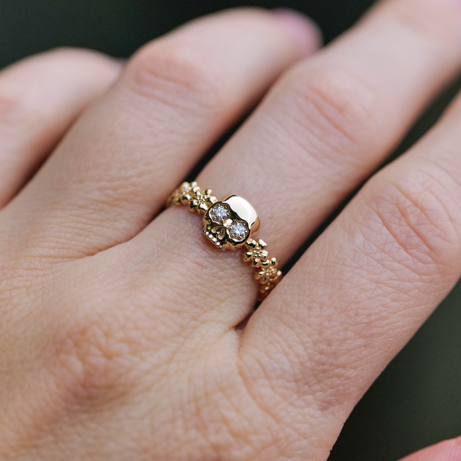 Forget Me Not Skull Ring by Fiat Lux—14k gold with gemstone eyes, shown in detail on the wearers finger.