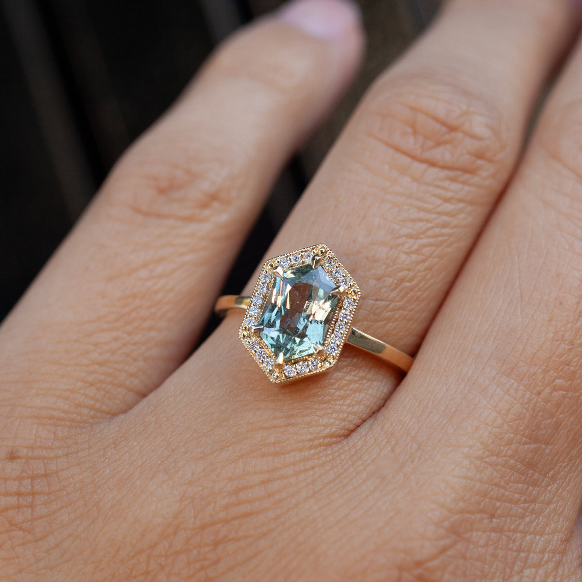 Fiat Lux Grande Hex Hester: a minty grey lavender hexagon sapphire ring with a diamond halo on an 18K yellow gold band.