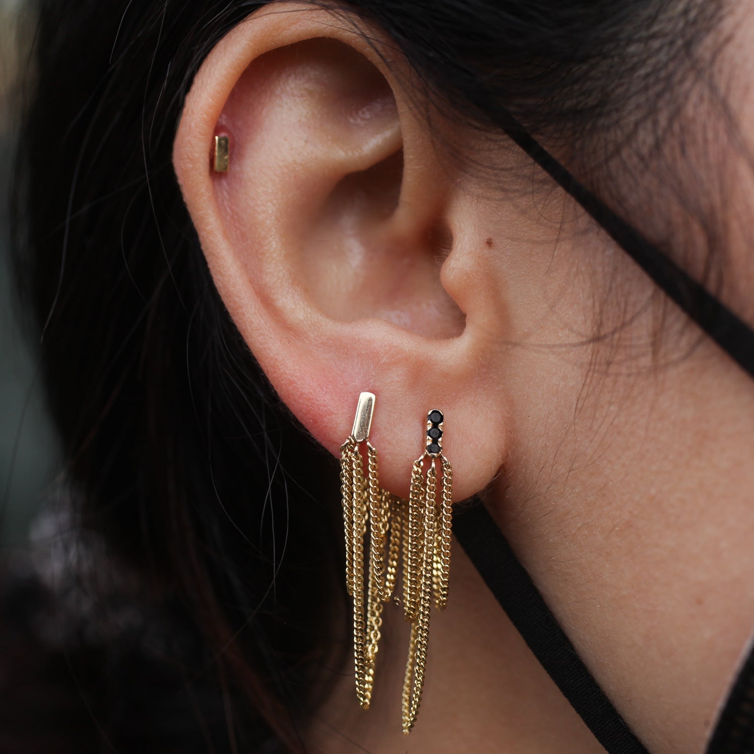 Close-up of an ear with Jack and G Chandelier Stud - Pavé and gold chain drops, person wearing a black mask.