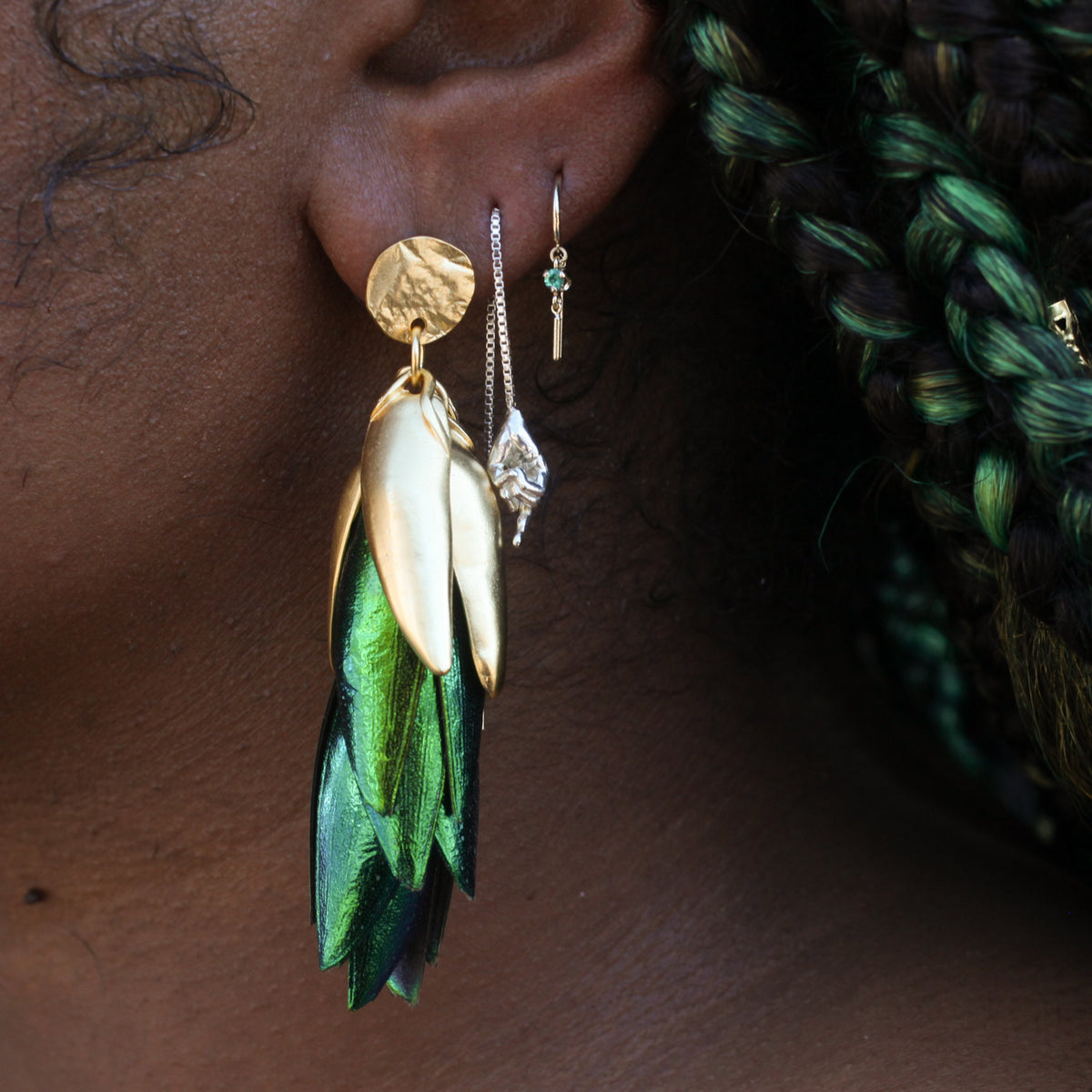 A person wearing 22K gold plated, iridescent beetle wing Figeater Chandelier Earrings and two smaller earrings.
