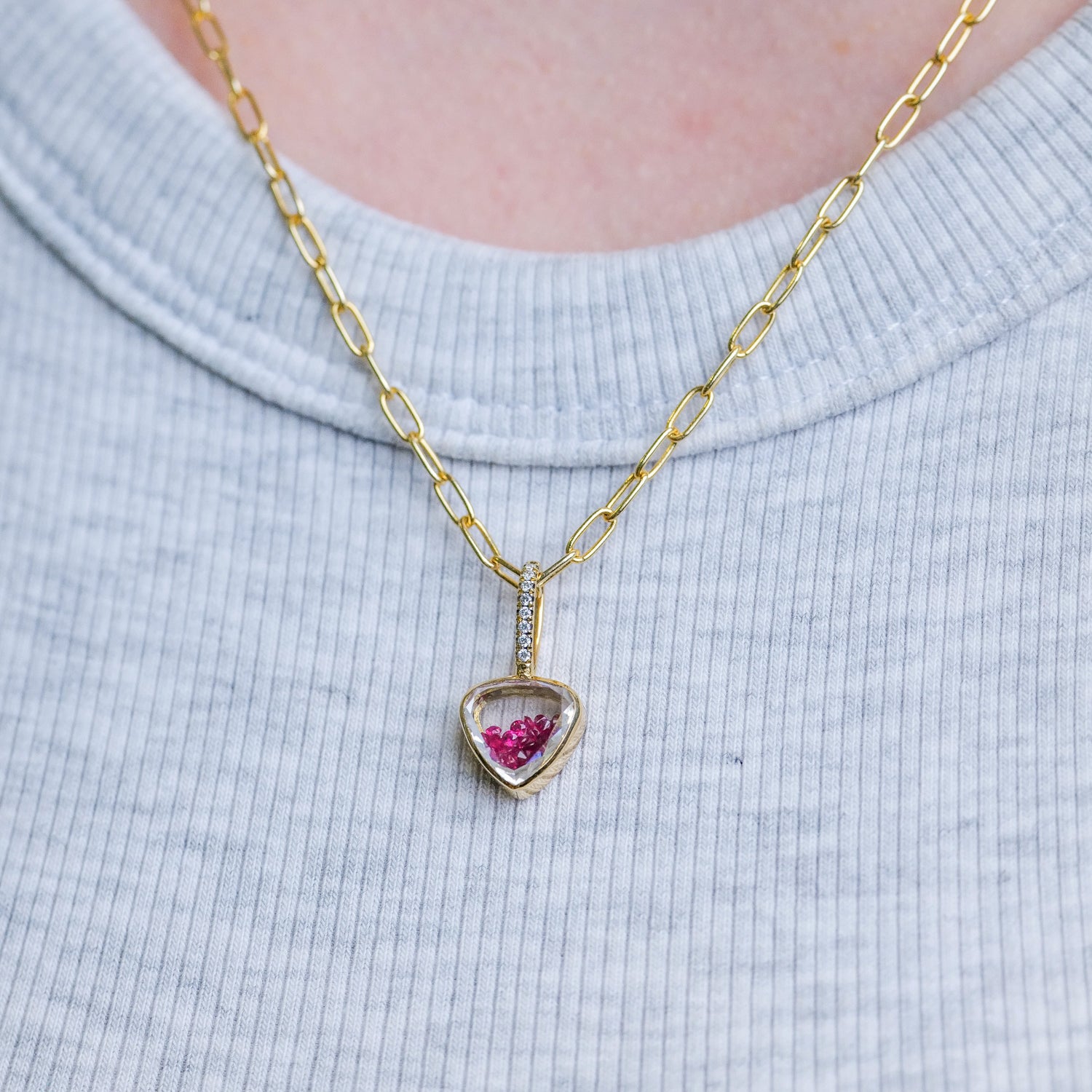 Moritz Gliks Naipe Heartish Pave Shaker Charm - Ruby on a gold chain, styled over a ribbed gray shirt.