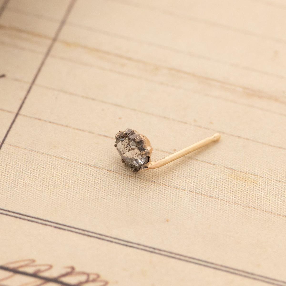 A Vintage Victorian Rose Cut Single Earring with a gold post resting on lined paper.