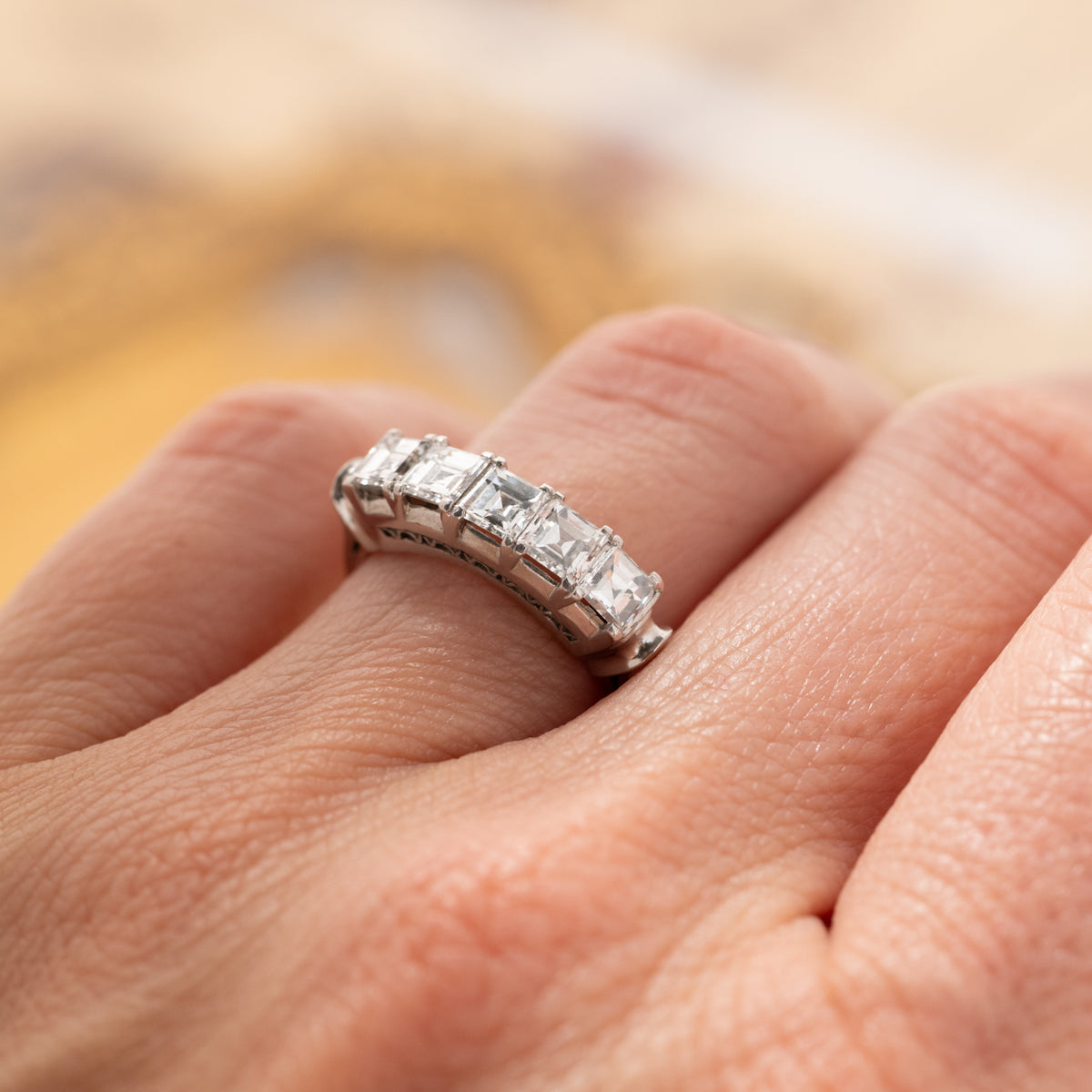 A hand wearing a Vintage Carré Cut Diamond Band - 4.5mm, a platinum ring featuring five square-cut diamonds in a row.