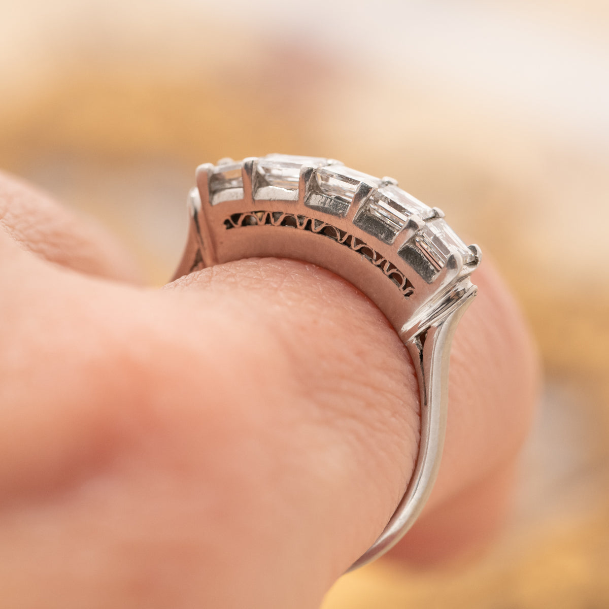 A finger wearing a Vintage Carré Cut Diamond Band - 4.5mm with five carre cut diamonds in an open-work platinum setting.