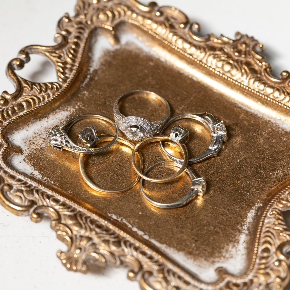 Vintage Transitional Cut Diamond Halo Ring and four other rings on an ornate, gold-toned rectangular tray.