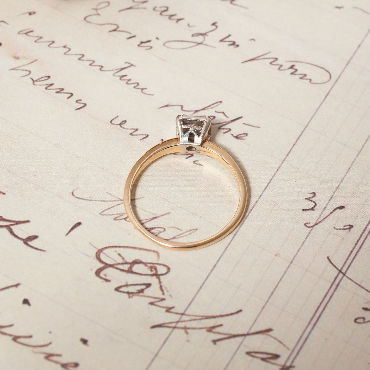 A Vintage Mixed Gold Diamond Solitaire Ring with a 14k gold band resting on vintage cursive handwriting.