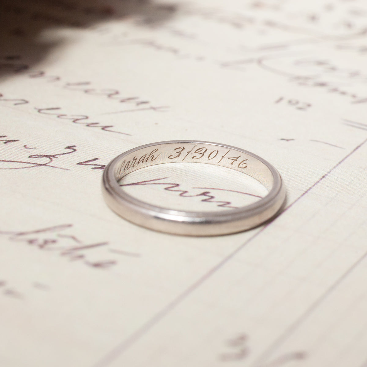 A Vintage Palladium Band engraved with Sarah 3/30/46 inside, resting on a handwritten document.