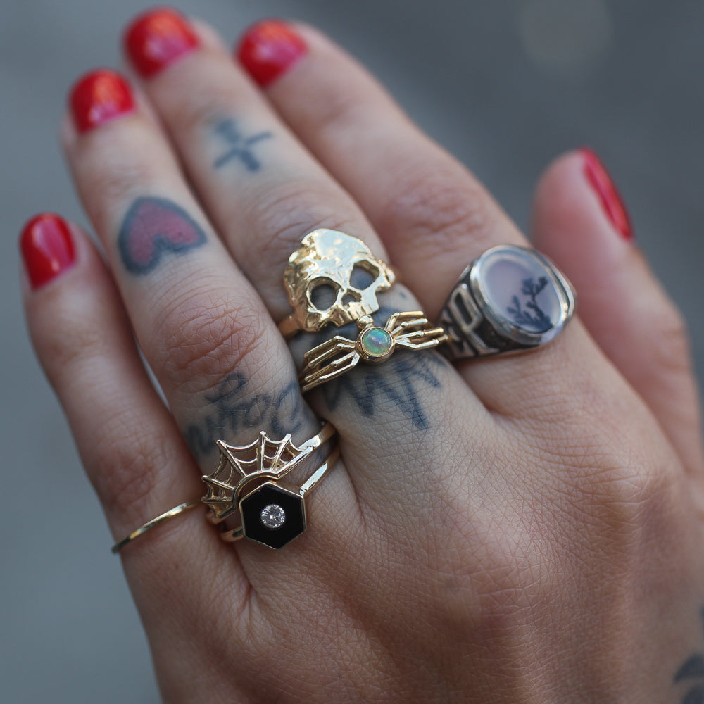 tattooed hand with six rings stacked in a horizontal array across four fingers with the dust to dust ring on the middle finger
