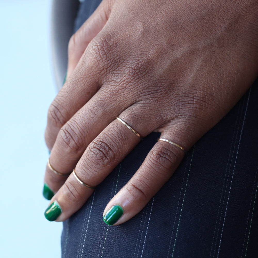 A hand placed on a thigh wearing two half cut rings on a midi finger setting and two full cut rings on the ring and pinky fingers