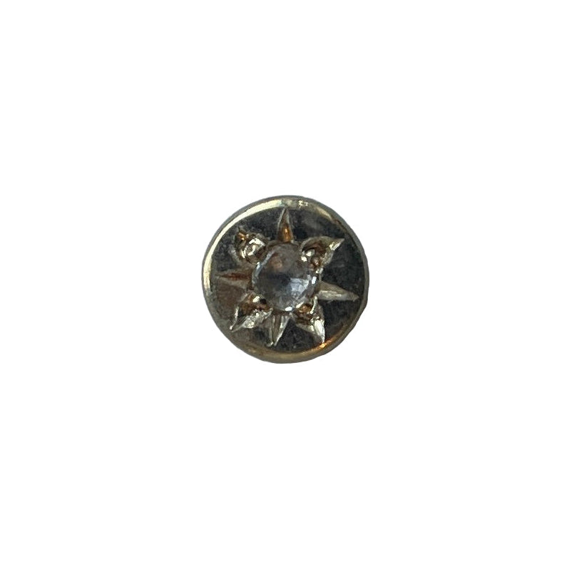 A gold-colored metal piercing with a clear central gemstone and intricate designs around it.