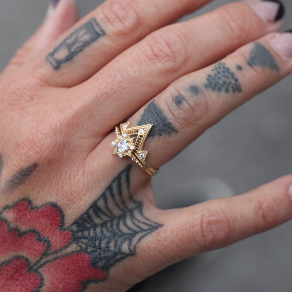 A slightly outstretched close up of a tattooed hand with A Giza Ring stacked on-top of another gold and diamond ring