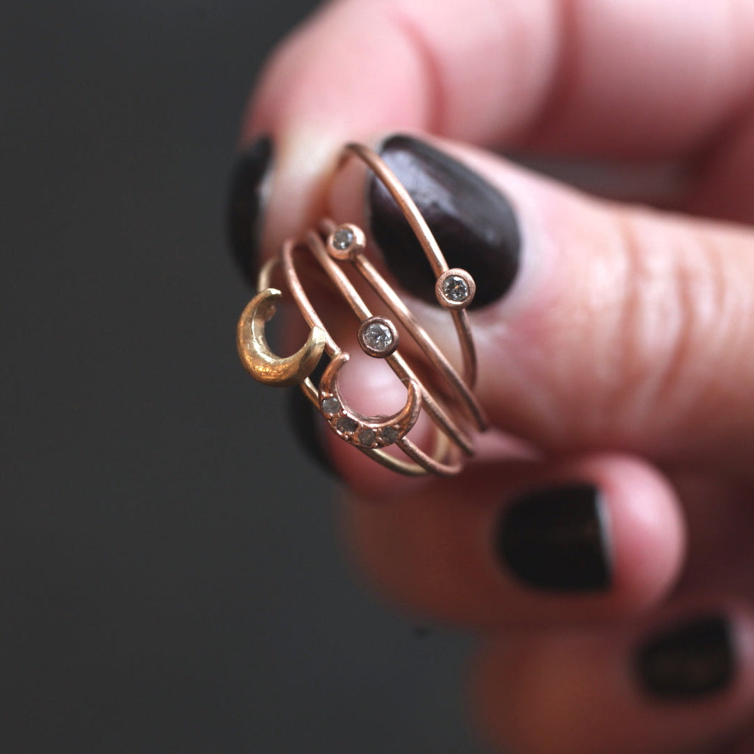 A hand with black nail polish holds the Daisy San Luis Pebble Ring (S), featuring crescent and round gemstone designs.